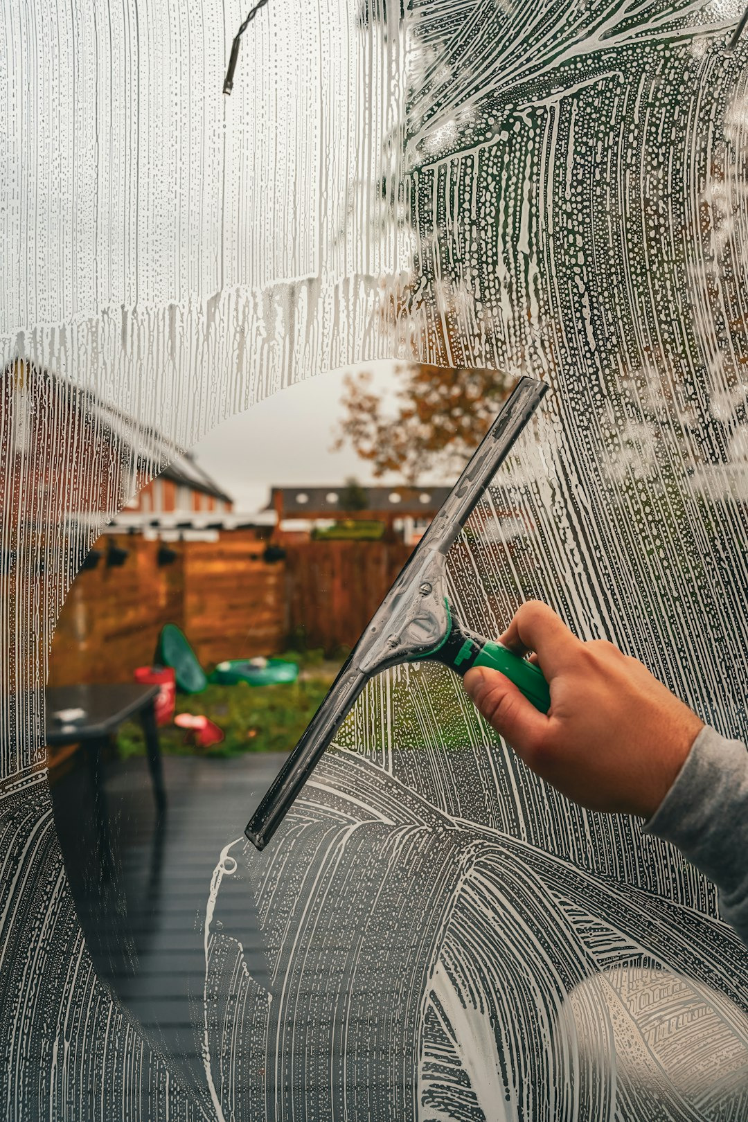 Hand mit Scheibenwischer reinigt ein Fenster