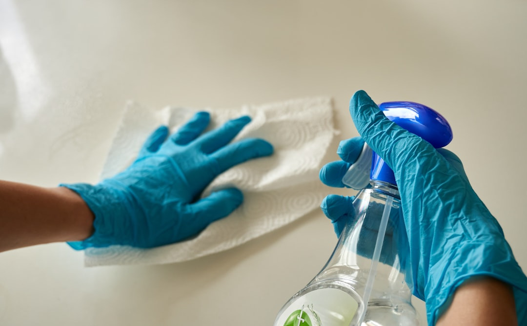 Hände in blauen Handschuhen halten eine Sprühflasche